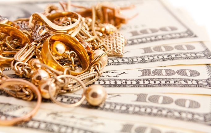 Gold rings, necklaces, and bracelets placed on top of $100 U.S. dollar bills, symbolizing cash for gold services at Ideal Jewelry & Loan