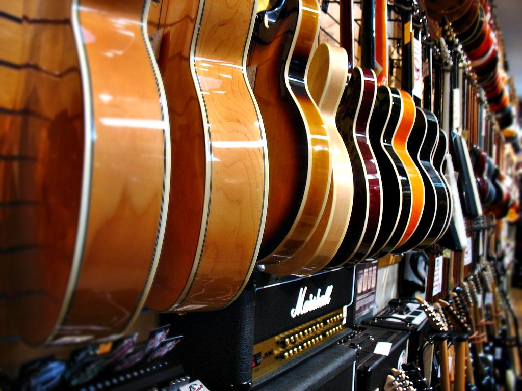 A variety of acoustic and hollow body guitars displayed at Ideal Jewelry and Loan pawn shop in Brockton, MA, above Marshall amps.