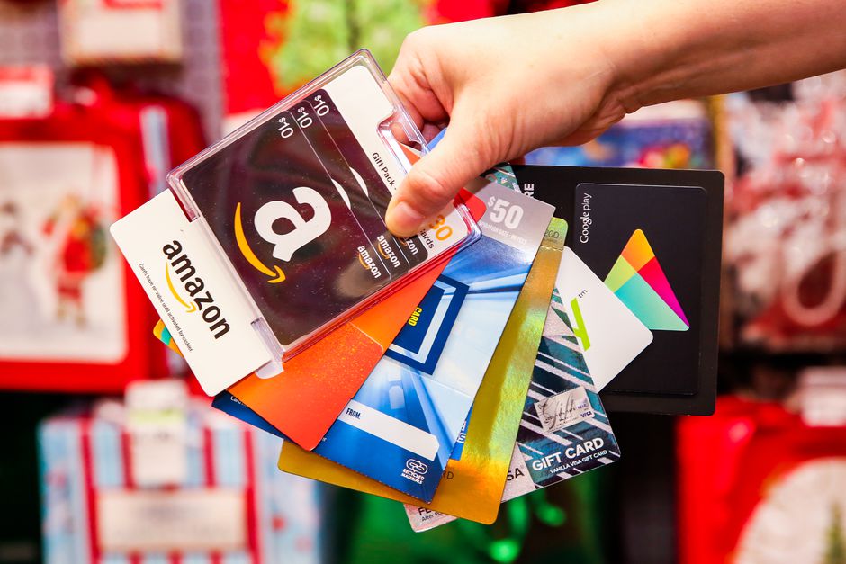A hand holding various gift cards including Amazon, Google Play, and Visa gift cards.