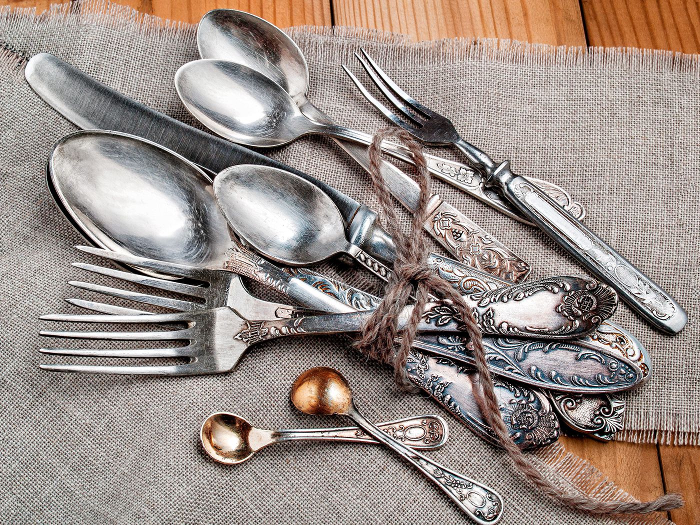 A rustic bundle of antique silverware including forks, spoons, and knives tied with twine on a burlap cloth.