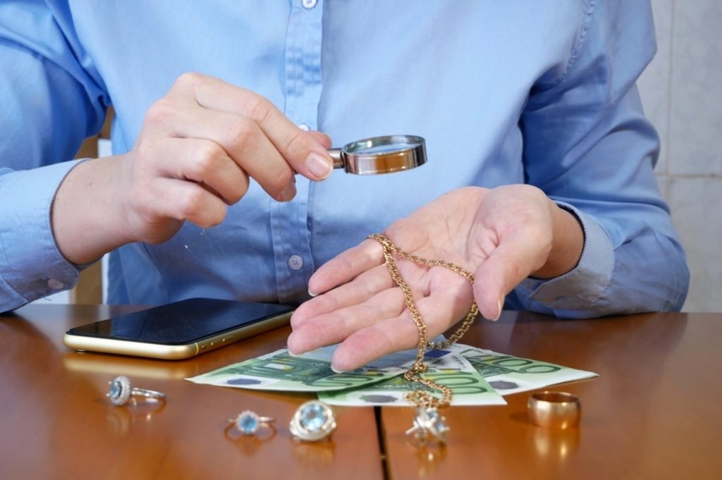 Jewelry appraiser inspecting gold chain with magnifying glass during loan assessment process