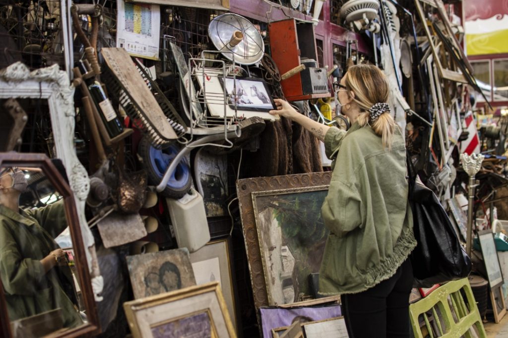 A woman browsing through a cluttered second-hand shop filled with vintage items, artwork, and antiques