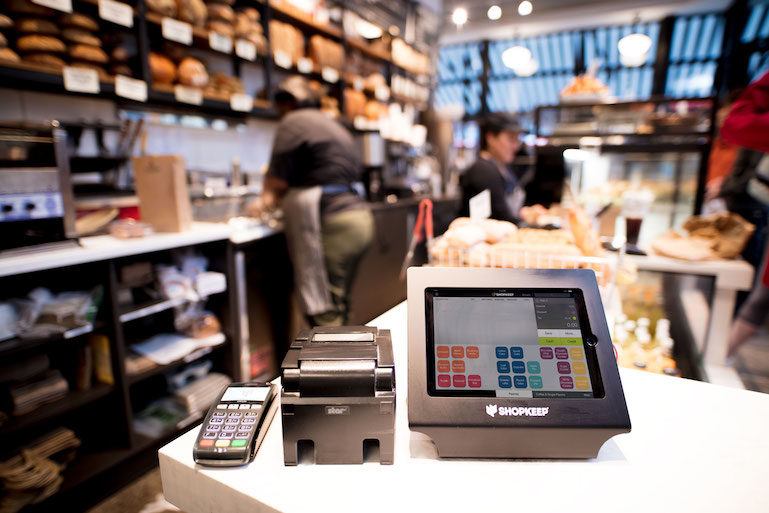 Modern point-of-sale (POS) system with touchscreen, receipt printer, and card reader in a busy shop environment