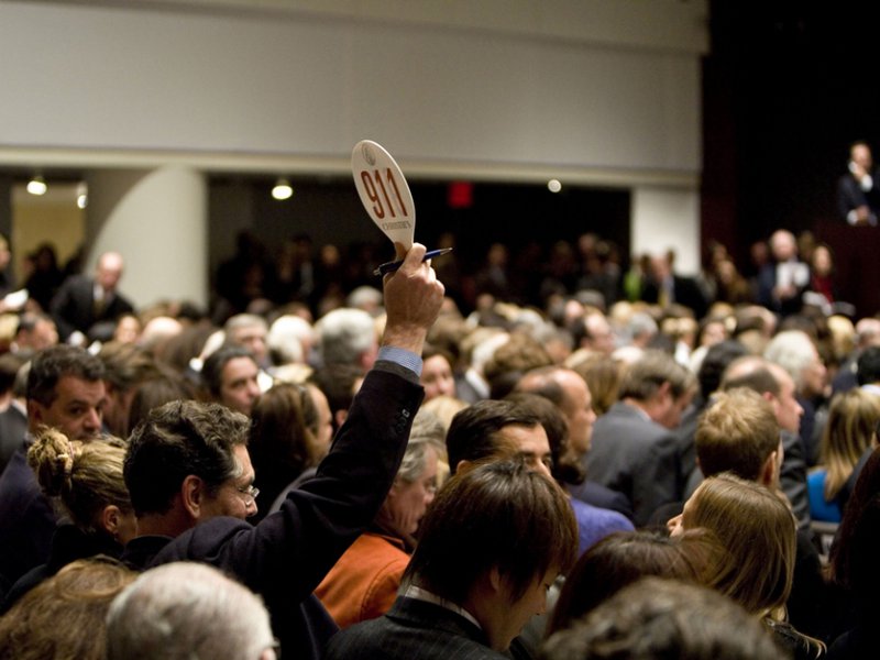 A person holding a numbered paddle in a crowded auction hall during a live pawnshop auction