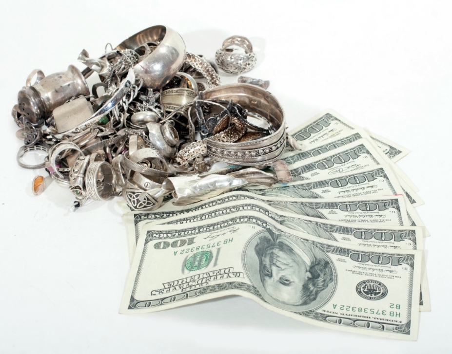 Pile of silver jewelry and accessories with hundred dollar bills underneath