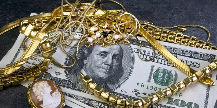 Gold jewelry and brooch laid over $100 bills on a dark background