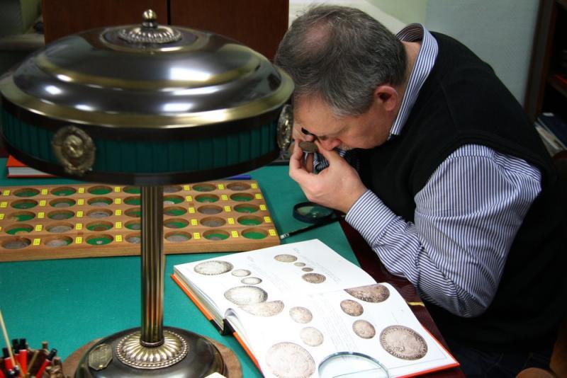 Coin dealer examining rare coins with a magnifier and reference book