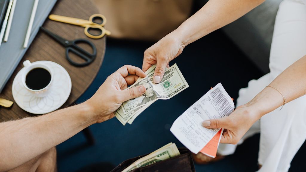 Person handing over cash and receipt during a transaction at a table with coffee and scissors