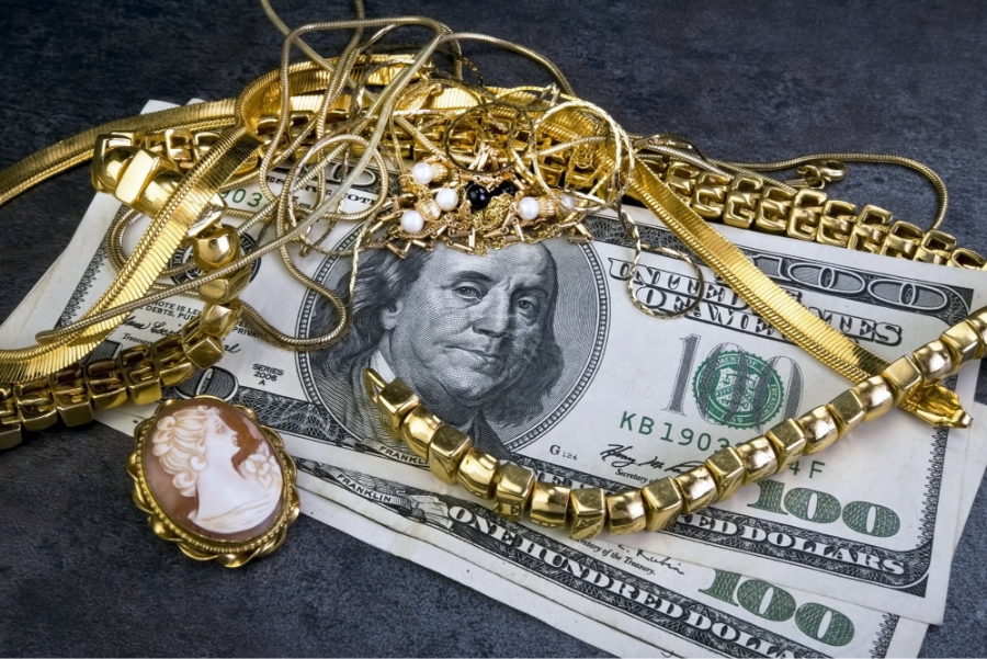 Gold jewelry and vintage brooch displayed over hundred‑dollar bills