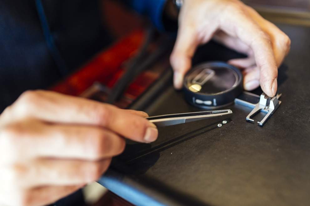 Close-up of hands examining small diamonds with tweezers and loupe on a jeweler’s table