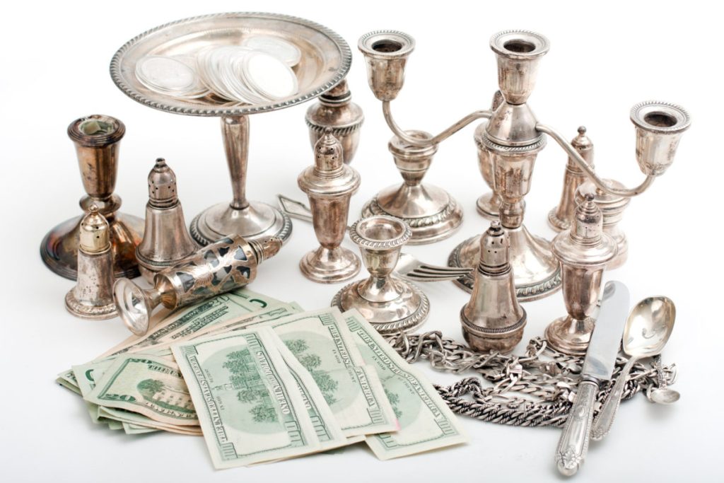 Silver antiques and flatware displayed with US dollar bills on a white surface