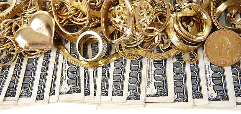 Gold jewelry and coins stacked over rows of hundred-dollar bills