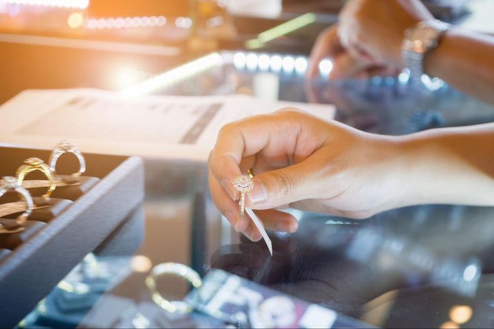 Hand holding a diamond engagement ring over a glass jewelry counter