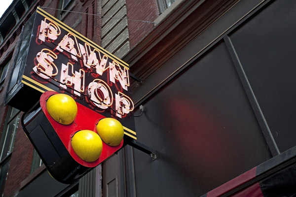 Neon pawn shop sign with three golden balls outside a building