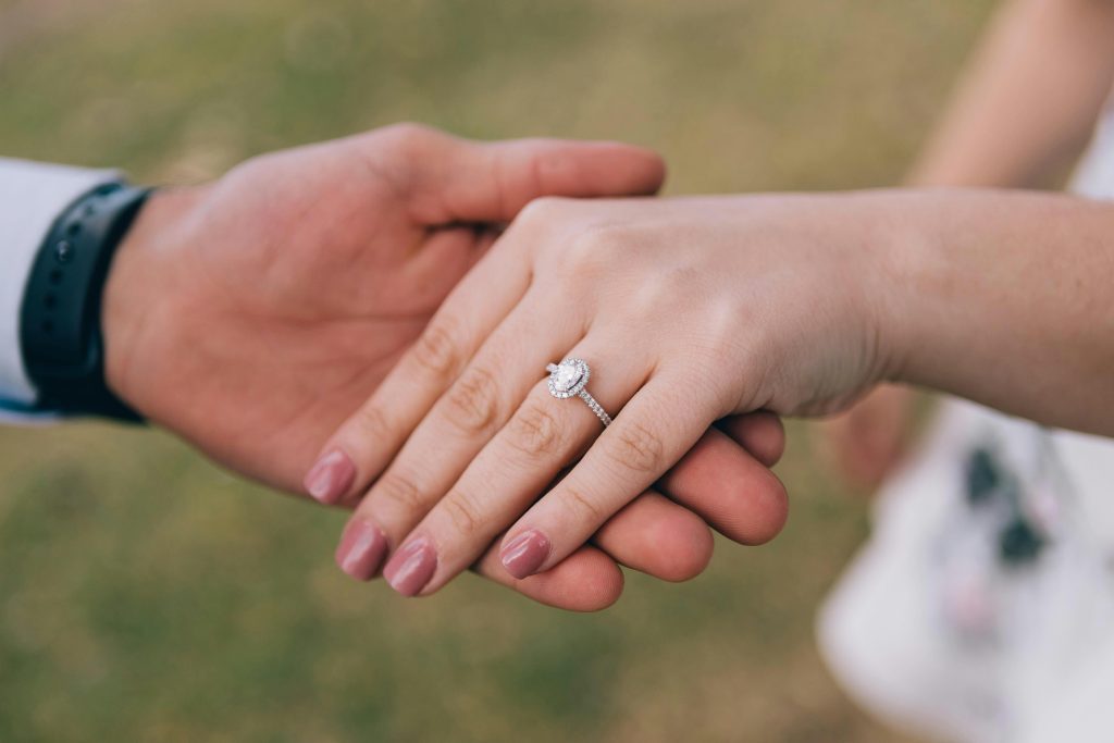 Hand wearing diamond engagement ring held by another hand.