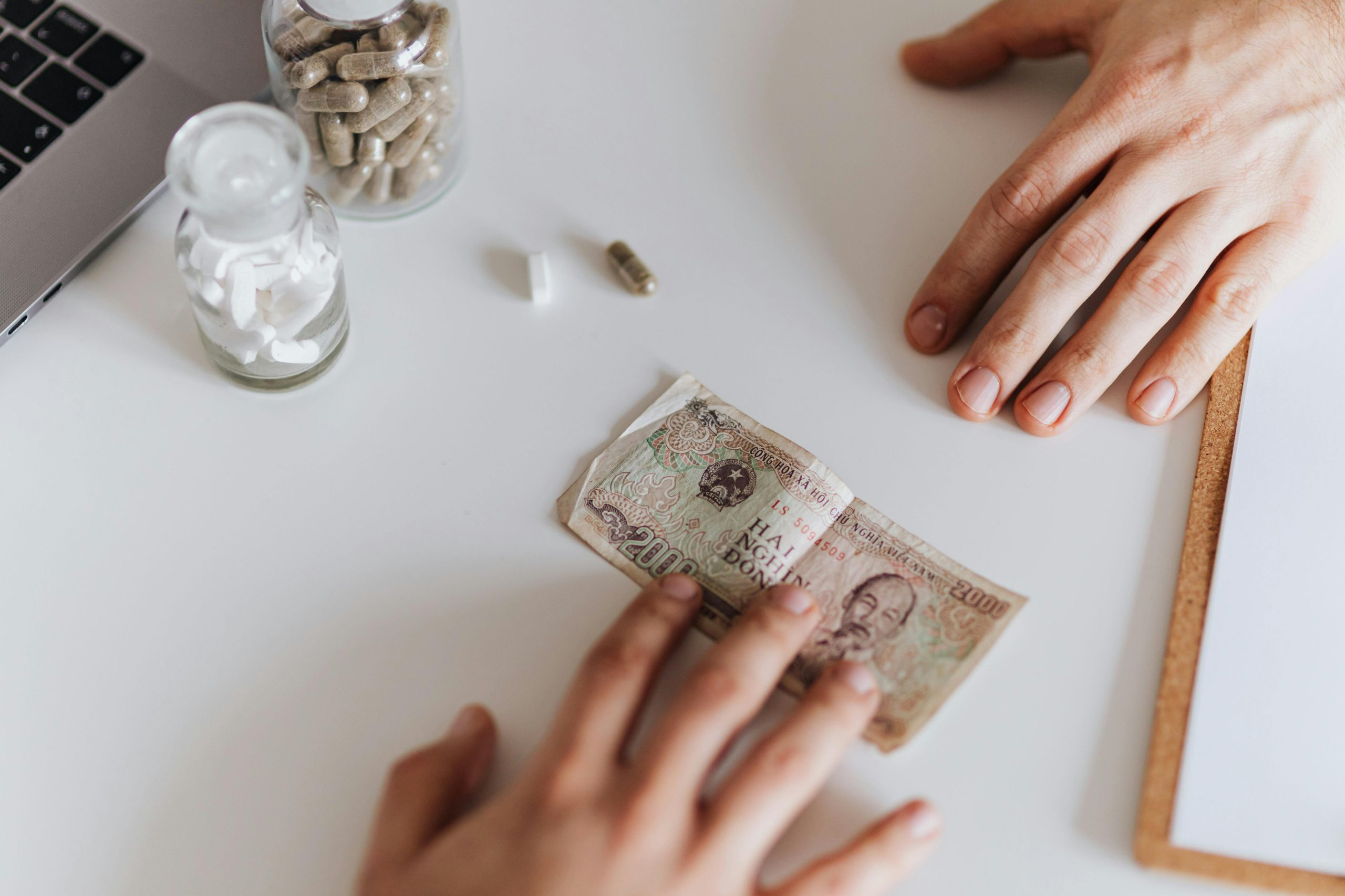 Hands exchanging currency note near supplement jars on white table.