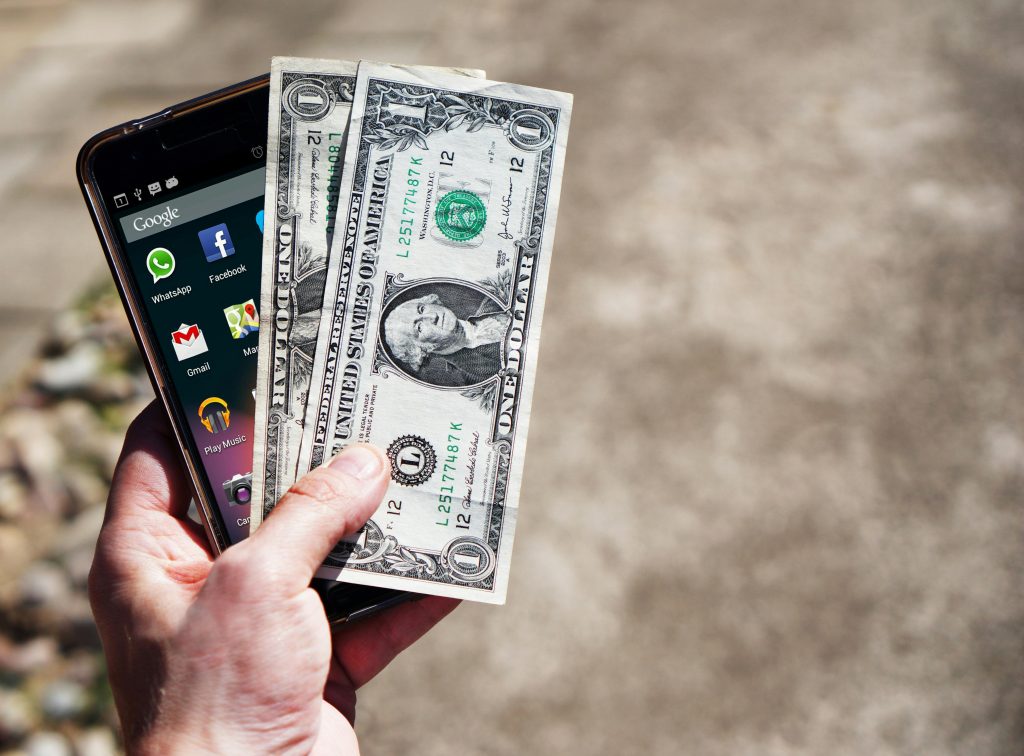 A hand holding cash and a smartphone symbolizing quick pawn shop transactions
