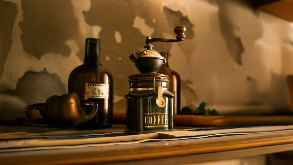 Antique manual coffee grinder with glass jar and vintage bottles on a rustic shelf
