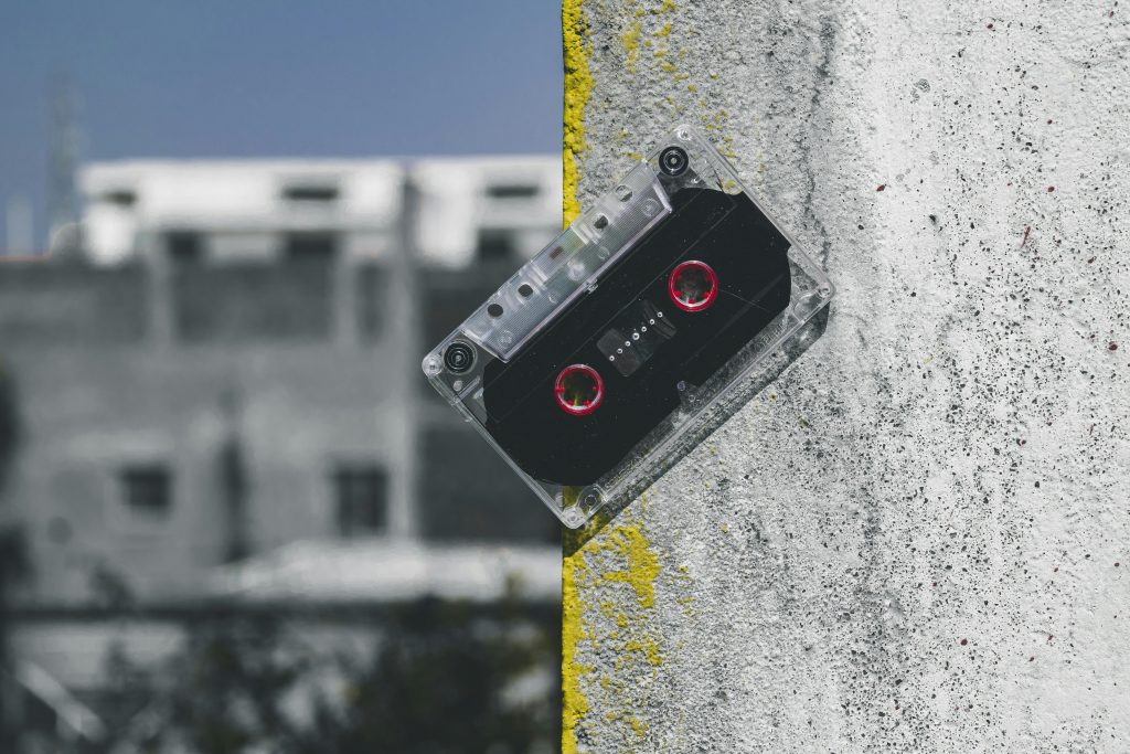 Clear plastic audio cassette with red reels leaning against a painted concrete wall, symbolizing retro items at pawn shops