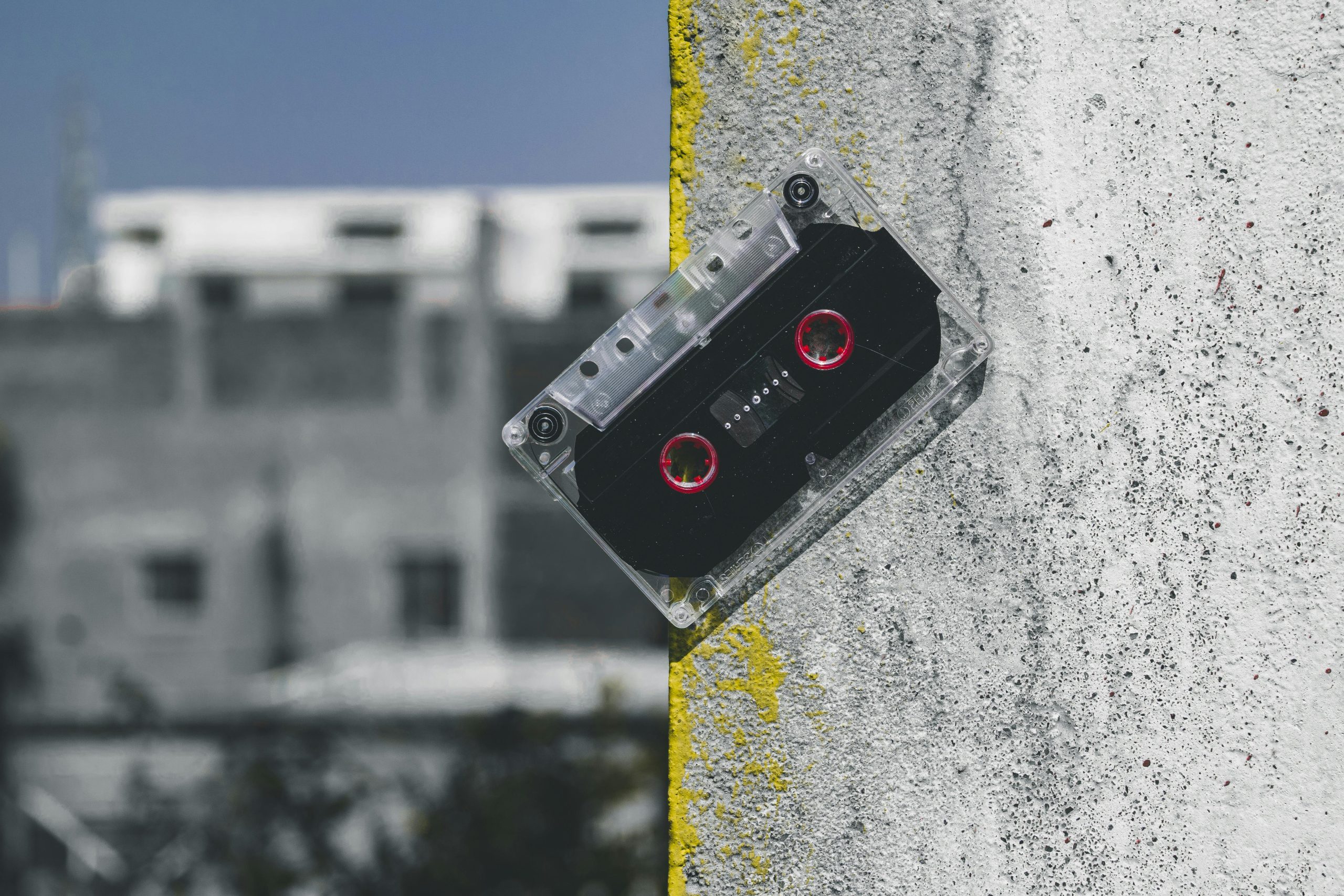 Clear plastic audio cassette with red reels leaning against a painted concrete wall, symbolizing retro items at pawn shops