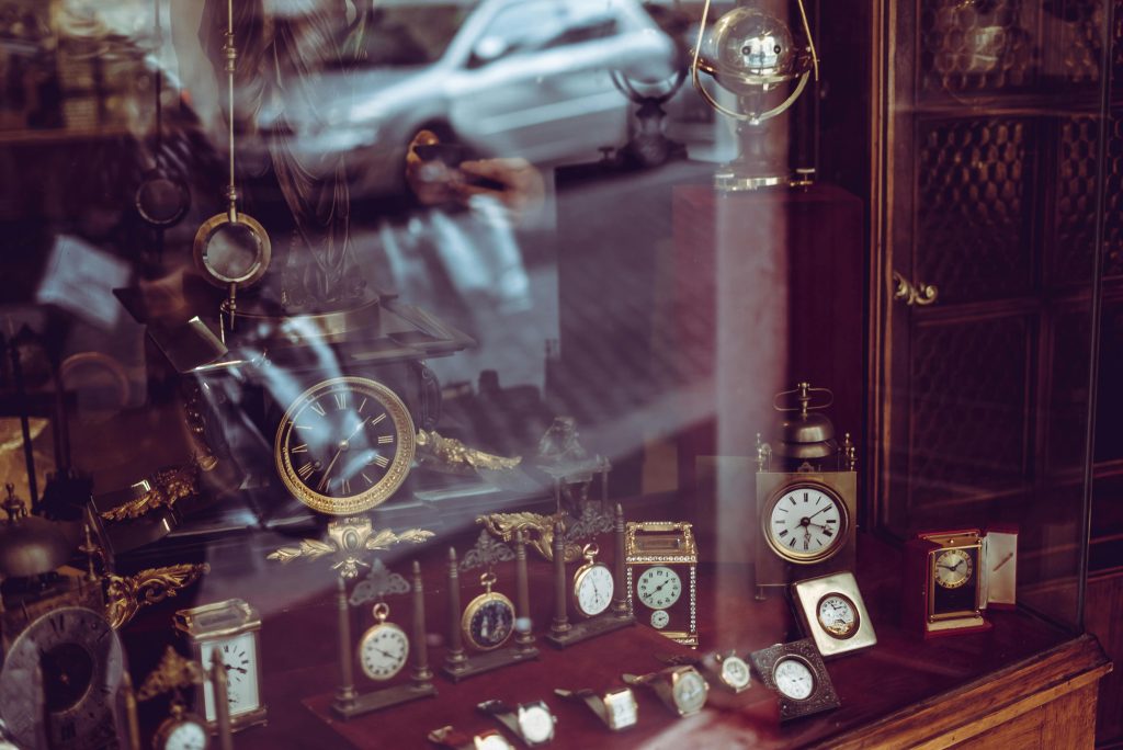 Display of vintage clocks and watches in a pawn shop window with reflections of the street outside