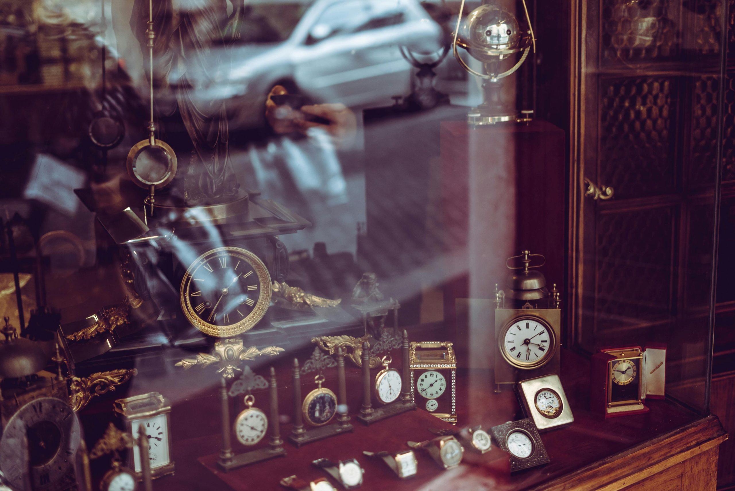 Display of vintage clocks and watches in a pawn shop window with reflections of the street outside