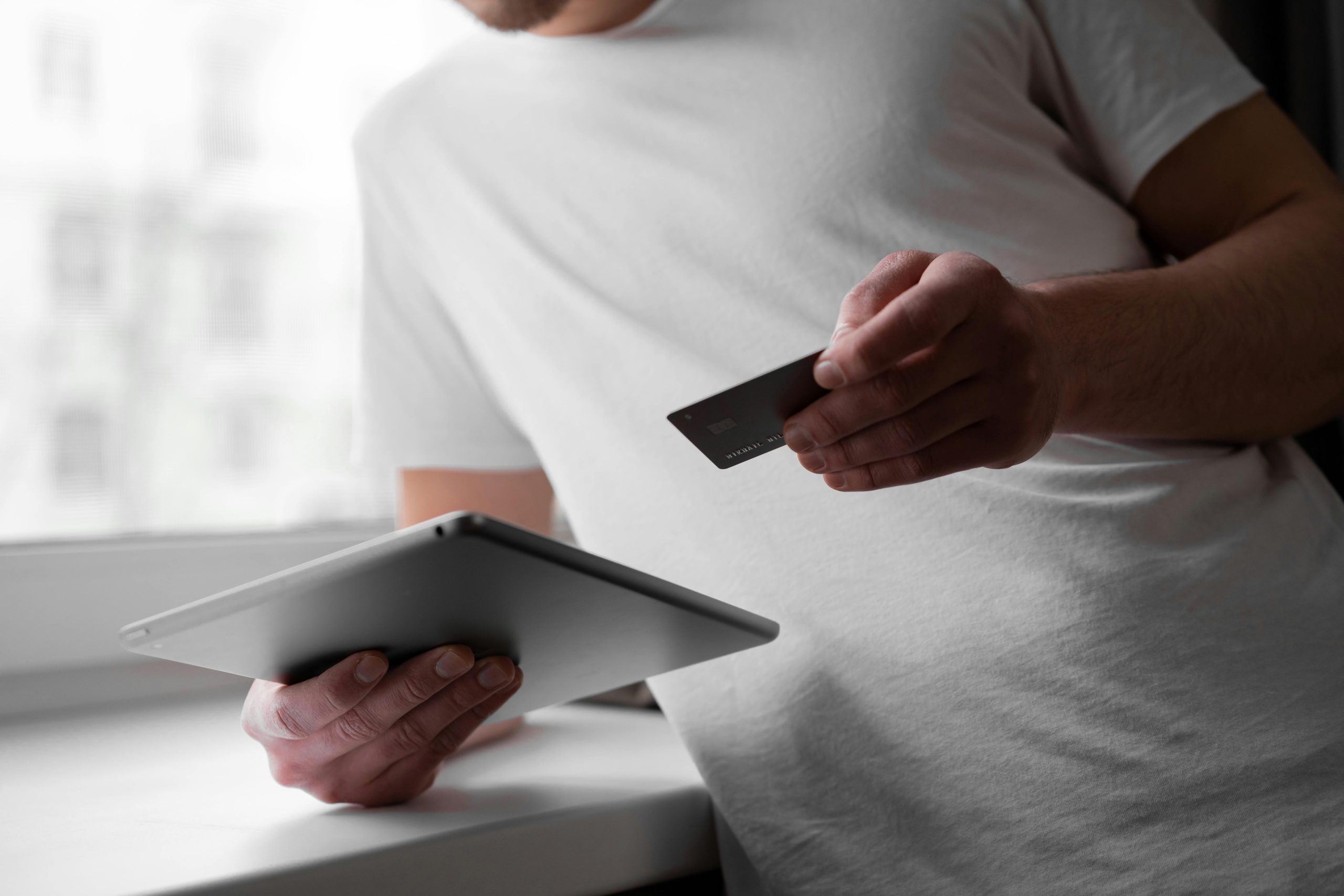 Man holding a credit card and tablet near a window, representing secure digital transactions at a pawn shop
