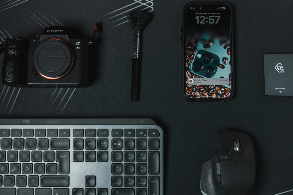 A DSLR camera, smartphone, keyboard, and accessories laid out on a dark surface, representing valuable electronics for pawn
